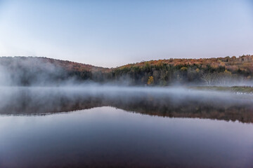 Fototapeta premium Spruce Knob Lake in West Virginia at sunrise with nobody and landscape view of blue water and forest trees in autumn fall season