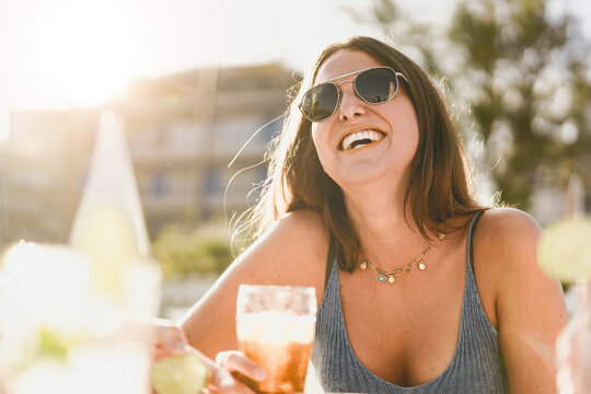 Portrait of an happy young woman with sunglasses having fun and drinking beer with friends at an outdoor cafe in the summer