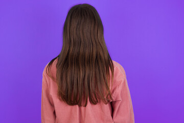 young beautiful Caucasian woman wearing casual clothes over purple wall standing backwards looking away with arms on body.