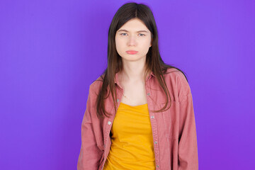 Fototapeta premium Gloomy, bored young beautiful Caucasian woman wearing casual clothes over purple wall frowns face looking up, being upset with so much talking hands down, feels tired and wants to leave.