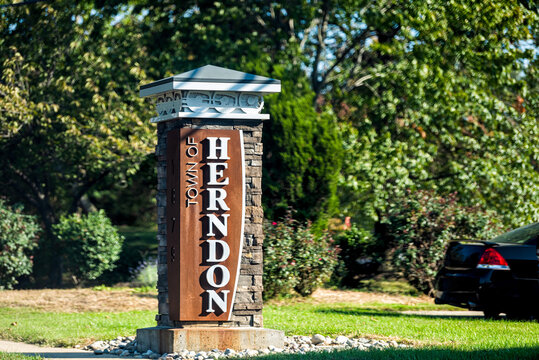 Stone sign for city or town of Herndon in Northern Virginia suburbs by green trees park near Washington DC
