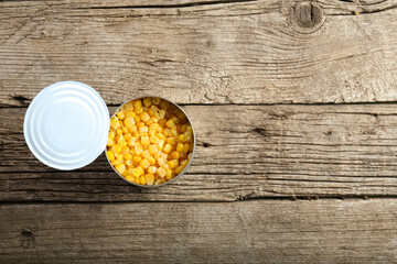 Open tin can with corn kernels on wooden background