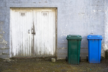 Blue recycle wheelie bin and green in row for collection outside factory