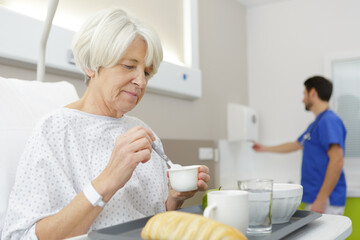 senior female patient eating meal in hospital bed