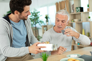 mature son congratulating elderly father giving him birthday gift