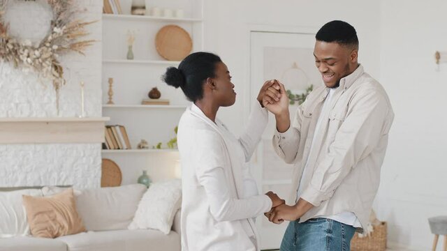 Happy african young parents afro married couple family pregnant woman wife and black man husband dancing at home enjoying pregnancy actively moving dance to music holding hands rejoice unborn child