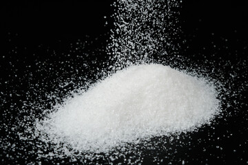 Heap of white sugar against black background. White granulated sugar drips onto the black surface.
