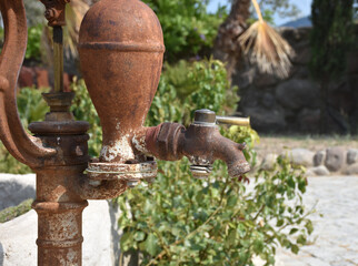 Old and rusty vintage water pump with stainless bucket.  traditional watering fountain in garden.