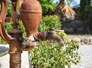 Old and rusty vintage water pump with stainless bucket.  traditional watering fountain in garden.