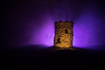 Obraz premium Stone defence tower at night. Medieval castle miniature with toned foggy backlight. Creative table decoration.