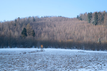 Hunting high stand on a snowy meadow near forest in winter
