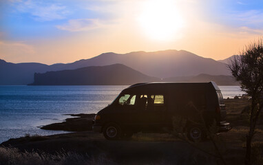Fototapeta na wymiar Minivan by the seashore at sunset against of mountains