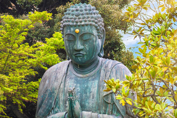 Close up on the bronze statue of Buddha Shaka Nyorai praying with two hands doing the gesture mudra called anjali in the Tendai Buddhism Tennoji temple in Yanaka cemetery