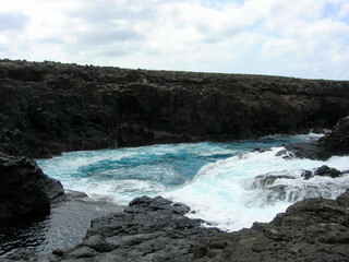 Small waterfalls left by the breaking wave on the dark rocks of Barracona, natural pool, Sal Island, Cape Verde