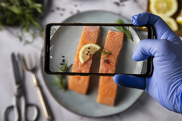 Top view of a hand in disposable gloves taking a picture of appetizing salmon fillets on the plate