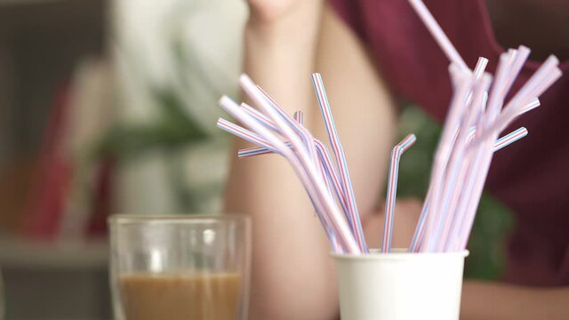 The girl takes a plastic tube for a cocktail with her hand. Say no to pollution, ecologists and the environment. Plastic striped straws.