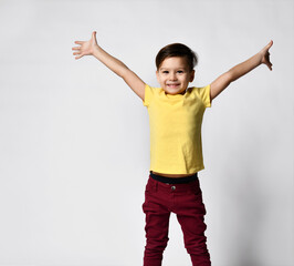 portrait of fashionable preschool little boy in yellow t-shirt, red denim pants, joyfully spread his arms out to the sides