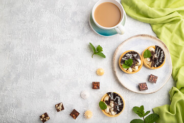 Sweet tartlets with chocolate and cheese cream with cup of coffee on a gray concrete background. flat lay, copy space.