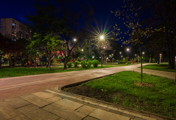 The tiled road in the night green park with lanterns in autumn. Benches in the park during the spring season at night. Illumination of a park road with lanterns at night. Park Kyoto
