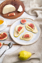 Summer appetizer with pear, cottage cheese, figs and honey on a white wooden background. Side view.
