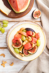 Vegetarian fruit salad of watermelon, grapes, figs, pear, orange, cashew on white wooden background. Top view, close up.