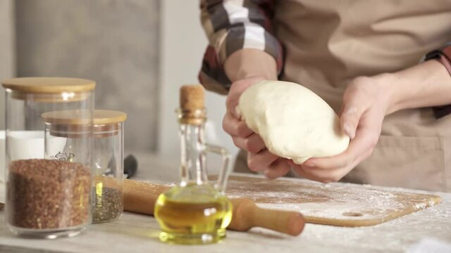 Chef baker kneading the dough with his bare hands. A baker chef kneads cream colored dough in a bakery kitchen to make homemade cakes.