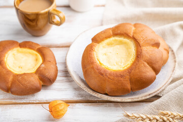 Sour cream bun with cup of coffee on a white wooden background. Side view, selective focus.