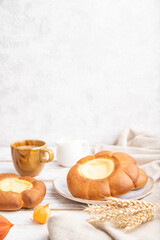Sour cream bun with cup of coffee on a white wooden and concrete background. Side view, selective focus, copy space.