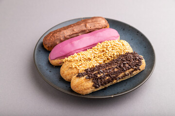 Set of eclair, traditional french dessert on blue ceramic plate on gray pastel background. side view, close up.