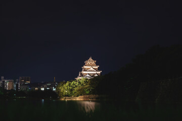 Fototapeta premium The illuminated Hiroshima castle surrounded by water in the cityscape at night, Hiroshima, Japan