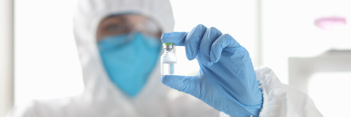 Scientists in protective suit respirators holding vial of vaccine in lab