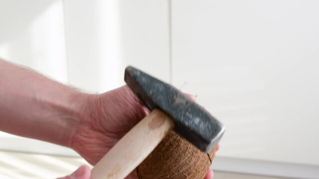 Man opens coconut by hitting it with hammer. Lifehack or method how to open coconut at domestic.