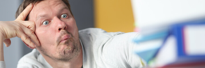 Obraz premium Tired man siting at table with many paper folders