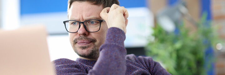 Disgruntled man with glasses looking at laptop screen