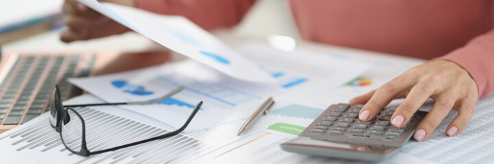 Business woman counting on calculator and holding documents in hands closeup