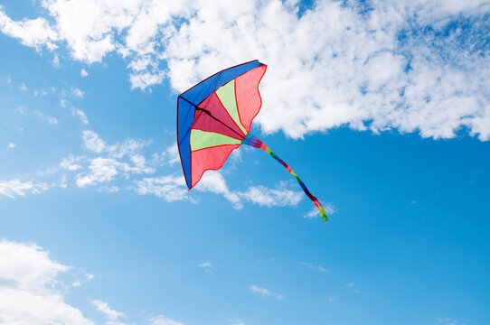 Colorful bright rainbow kite hovering in the blue sky with white clouds