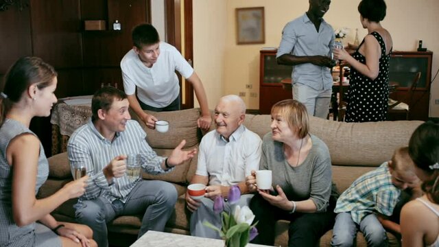 Big happy multiethnic family gathering in parental home, cheerfully talking together in living room