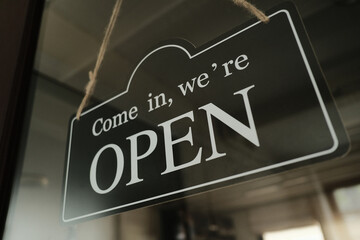 Open sign hanging on the glass door of a small business shop. Cafe and restaurant sigboard. Film grain effect.