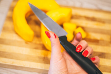 Female hand with red manicure holds knife with wounded hand, on background of cutting board with pumpkin