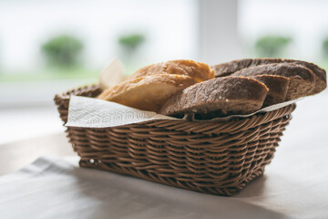 Wicker basket with black and white bread on white tablecloth near the window