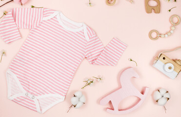 pink bodysuit, bear and accessories for newborn boy on pink table. Mockup of infant bodysuit from organic cotton with eco friendly wooden toys. Baby shower, festival, birthday decoration. Top view