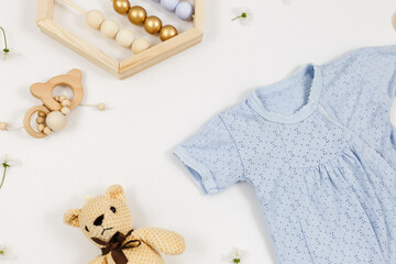 Blue bodysuit, bear and accessories for newborn boy on white table. Mockup of infant bodysuit from organic cotton with eco friendly wooden toys. Baby shower, festival, birthday decoration. Top view