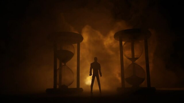 Time concept. Silhouette of a man standing between hourglasses with smoke and lights on a dark background. Surreal decorated picture