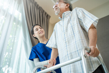 Obraz premium Asian female therapist helping senior male patient to practice walking