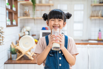 Portrait of Asian little young girl drinking milk in the kitchen.