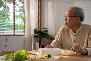Asian old man eating food, sitting alone on dining table at home.	