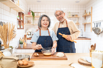 Obraz na płótnie Canvas Portrait of Asian senior couple standing in the kitchen cooking bakery