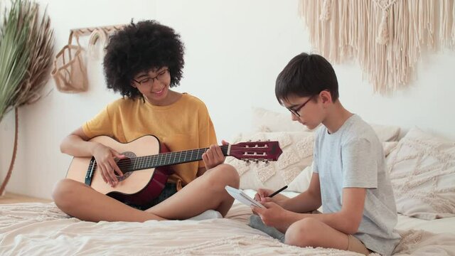 Music Teaching, Musical Education, Playing Guitar, Time Together. Girl teaches boy to play guitar while sitting on bed at home