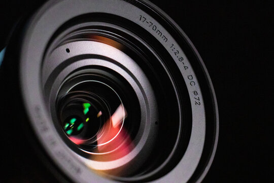 Close up of a camera lens lit with a soft light. There are red and green colors being reflected in the surface of the glass.  There is a black background.