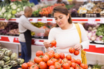 Obraz premium Beautiful latin woman in produce section of supermarket with shop worker in background